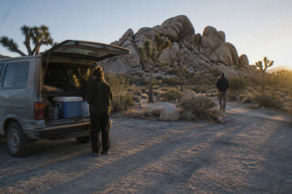 A parked van beside a rock formation in late afternoon light on a desert road