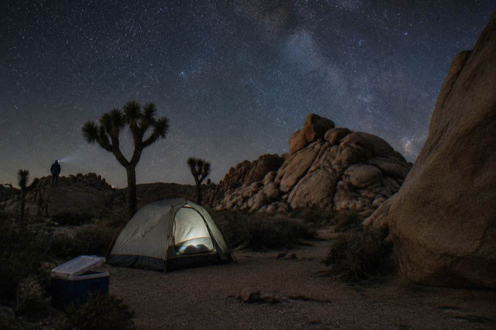 A desert campsite with a tent pitched among boulders under a star-filled night sky
