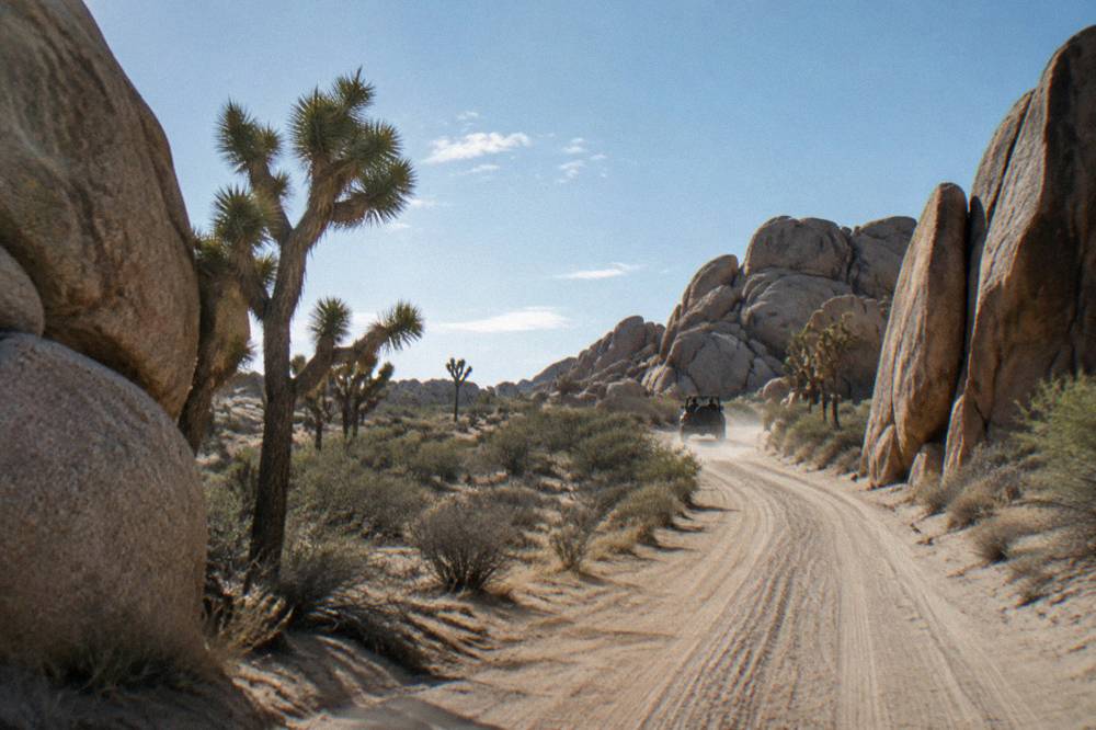 A dirt track winding between tall granite formations under a wide desert sky