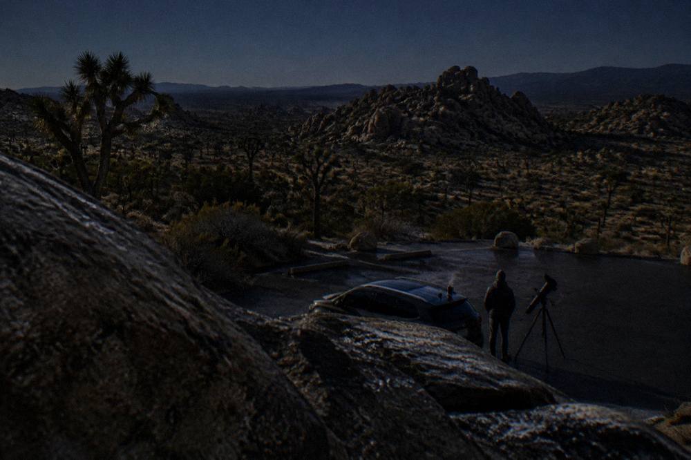 A parking area in the desert at night with a telescope silhouette against a starry sky