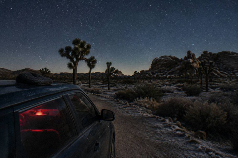 A parked car beside a desert road under a star-filled night sky