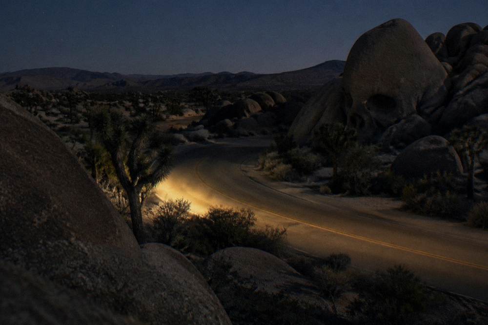 An empty paved desert road winding through dark rock formations at night