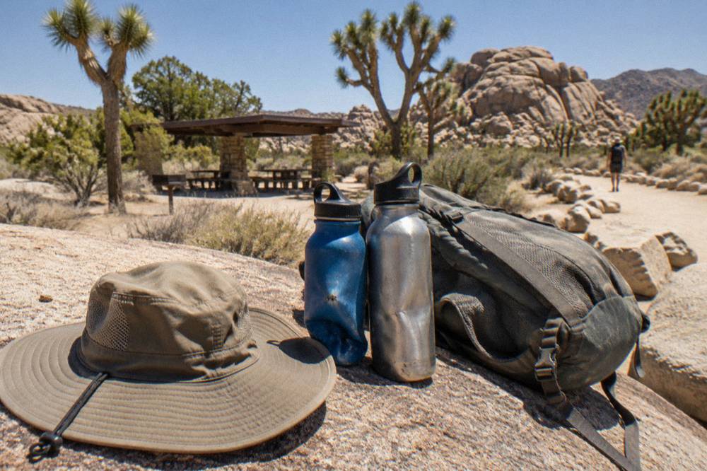 Sun hat, water bottles and a daypack resting on a rock beside a desert trail