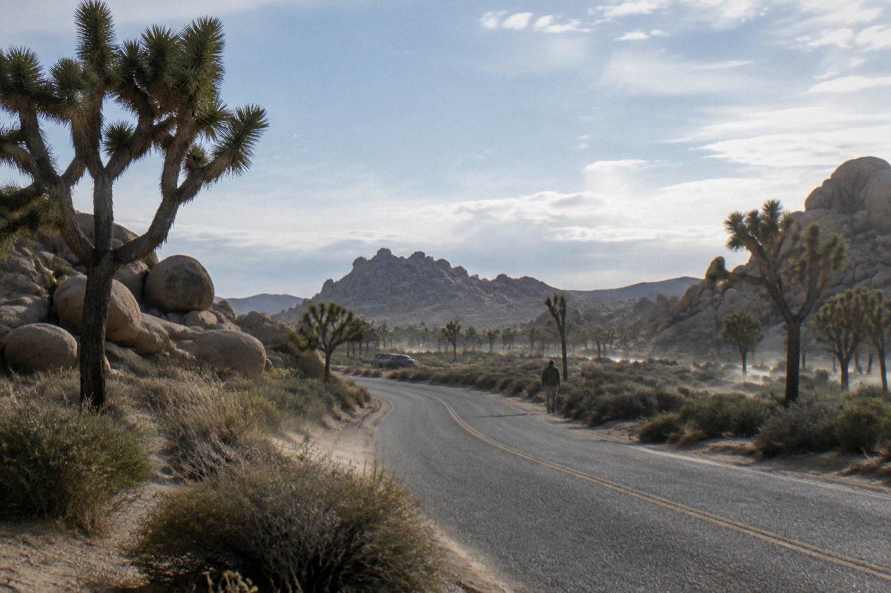 Empty desert road curving between boulder piles and Joshua trees under a wide sky