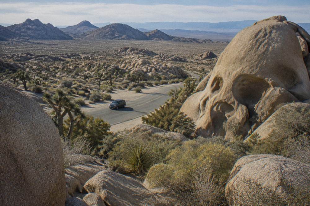 A granite boulder formation beside a paved park road with desert plain beyond