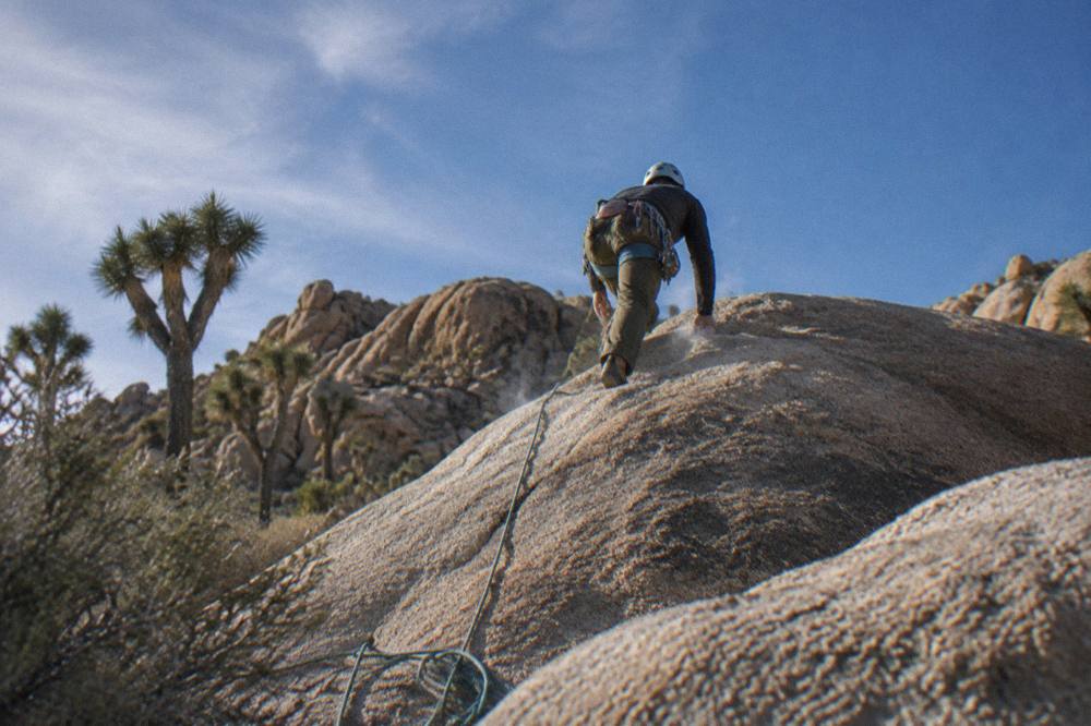 A climber on a granite boulder face with a rope and helmet in bright desert light