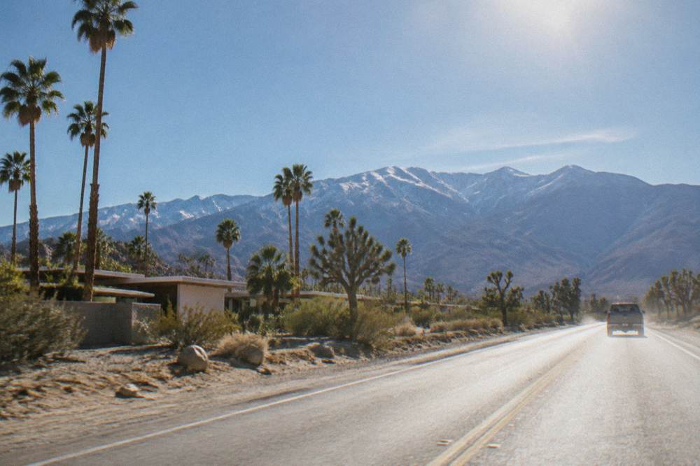 A desert highway heading toward distant mountains with open scrubland on both sides under a clear sky