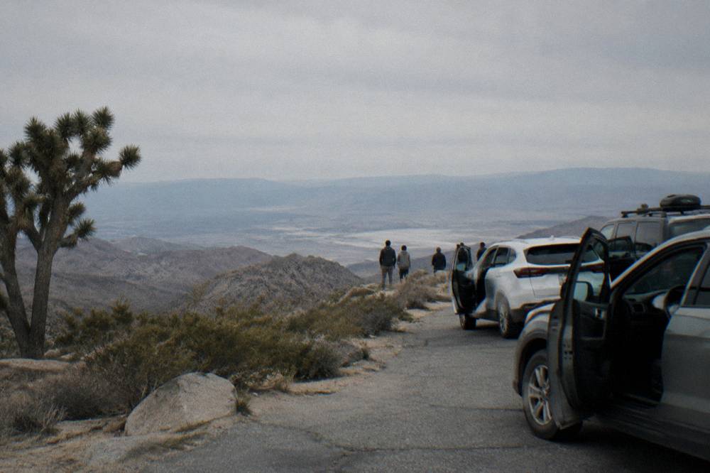 A line of cars parked at a crowded desert overlook with rock formations in the background