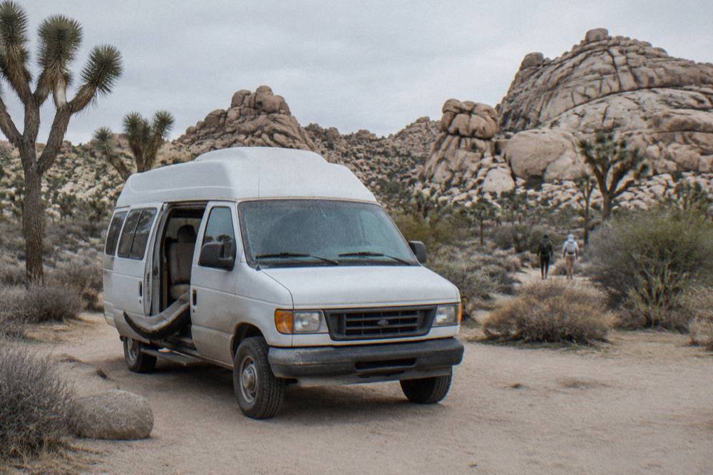 Tour van parked at a desert overlook with rock piles in the distance