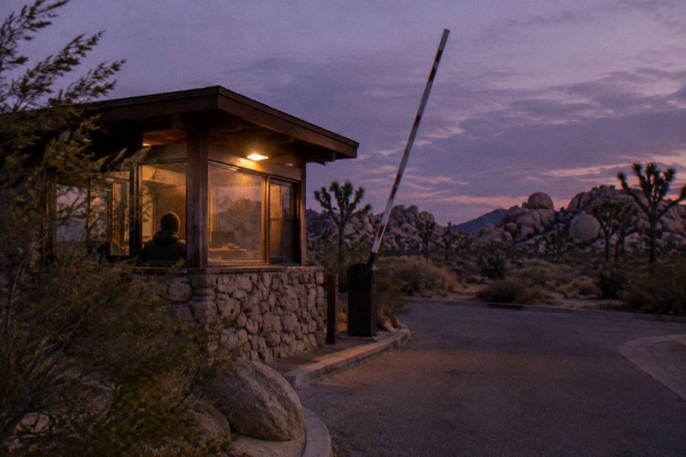Entrance station sign beside a desert road with scattered boulders
