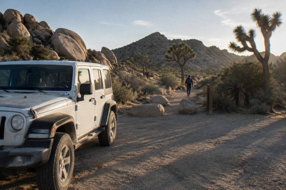 White jeep parked on a dirt road beside large granite boulders