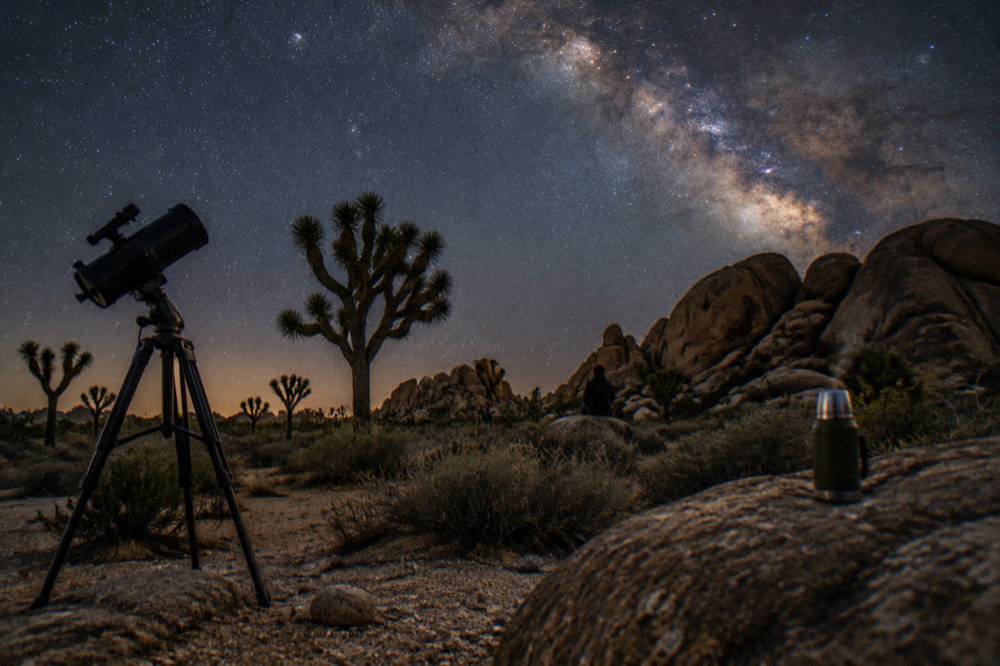 A telescope silhouetted against a bright band of the Milky Way over the desert