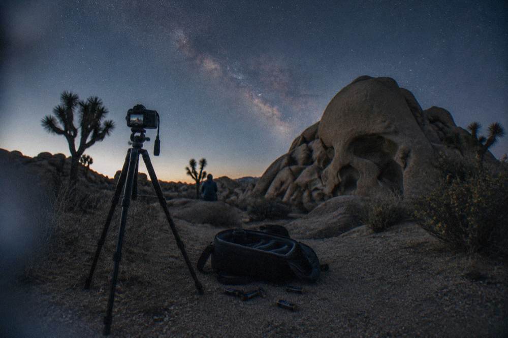 Camera on a tripod pointed at the Milky Way above desert rocks