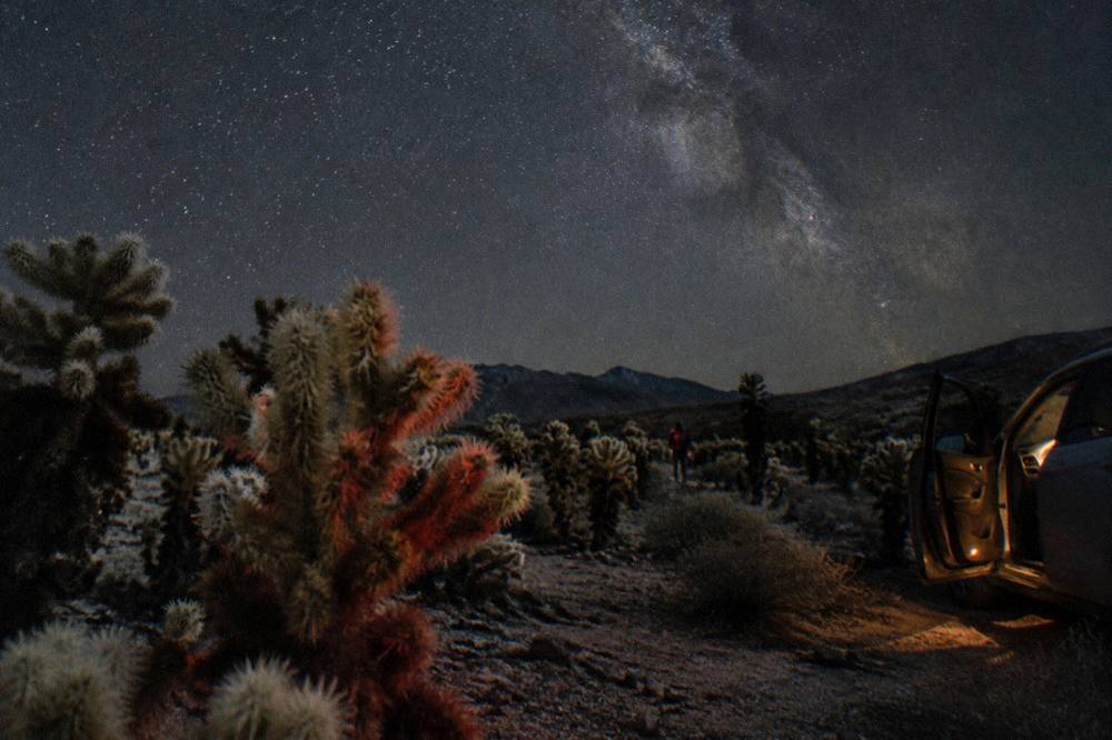 Red headlamp glow beside a parked car under the Milky Way