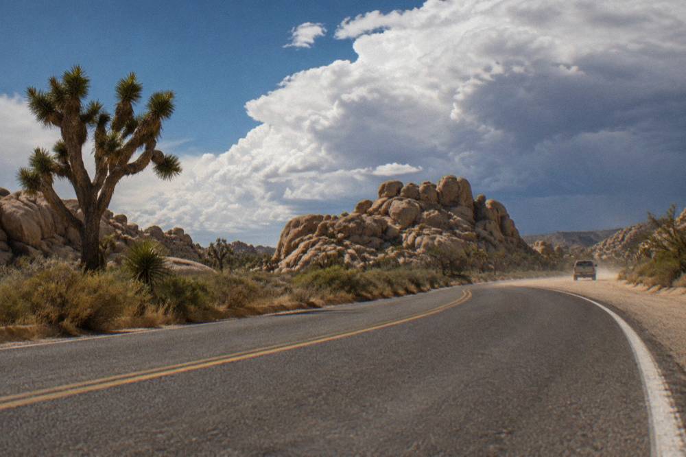 A paved desert road curving between large rock piles under a wide sky