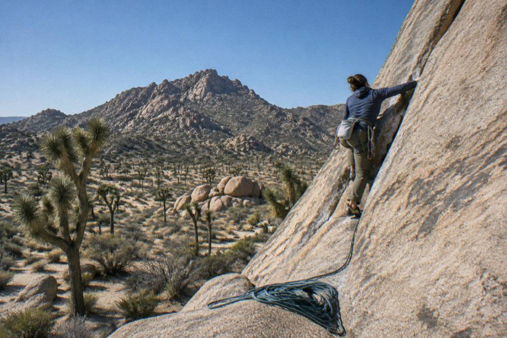 A rock climber on a granite boulder face beneath a clear blue desert sky
