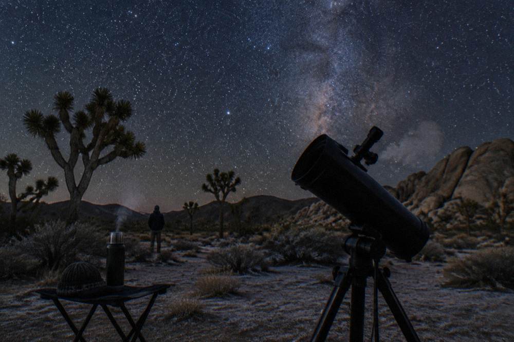 A telescope silhouetted against a star-filled night sky over the desert